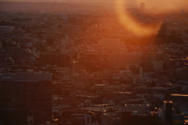 The suns golden rays reflect off buildings in a sprawling hazy city during sunset or sunrise