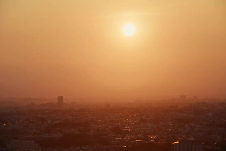 The sun shines through thick haze over a city