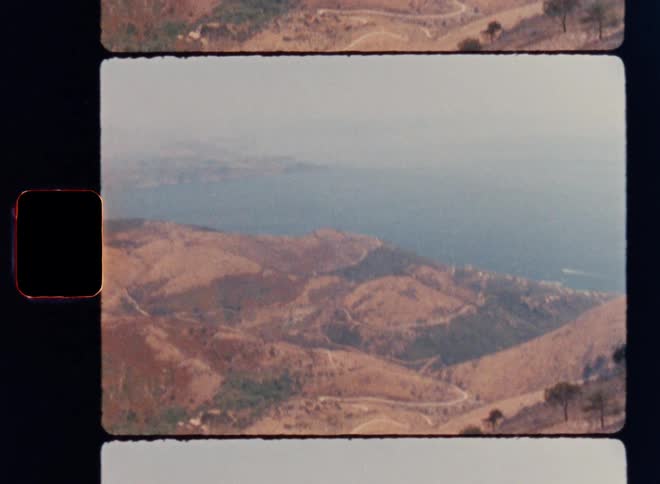Sweeping Super 8mm panoramic tilt revealing a winding mountain road, dry sun-bleached hills and a distant calm blue sea, captured in vintage analog film with grain, sprocket borders and a warm nostalgic Mediterranean atmosphere