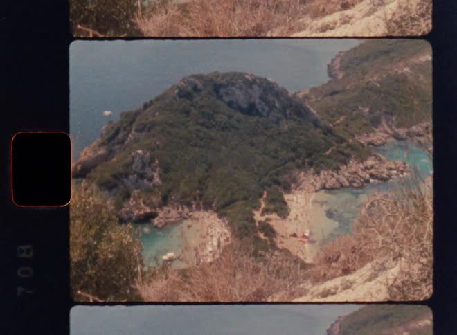 Cinematic Super 8mm handheld shot overlooking a lush green peninsula with twin turquoise coves, sandy beaches, rocky cliffs and boats below, captured from a high coastal viewpoint in warm vintage analog film style