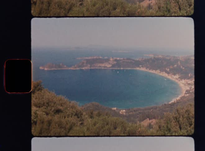 Cinematic Super 8mm coastal panorama capturing a forested hillside opening into a wide turquoise bay with sandy shoreline, distant islands, and calm blue waters as the camera slowly pans from the landscape toward the large crescent-shaped beach