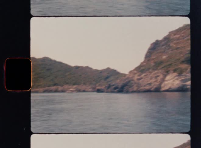 Cinematic Super 8mm coastal shot of a rocky, vegetation-covered island rising from calm blue water, captured from a sideways moving camera gliding past steep cliffs with vintage film grain, soft colors, and authentic analog texture