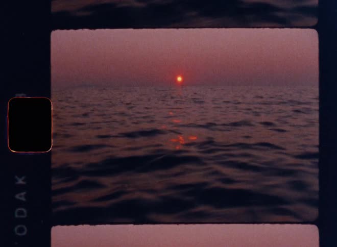 Cinematic Super 8mm sunset over gently rolling ocean waves, glowing red sun on the horizon casting shimmering reflections across the water, framed in vintage film strip borders with soft grain and warm nostalgic tones
