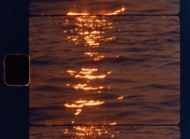 Cinematic Super 8mm close-up of golden sunset reflections shimmering across gentle ocean waves, capturing warm flickering light on rippling water with vintage film grain, nostalgic texture, and authentic analog film strip framing
