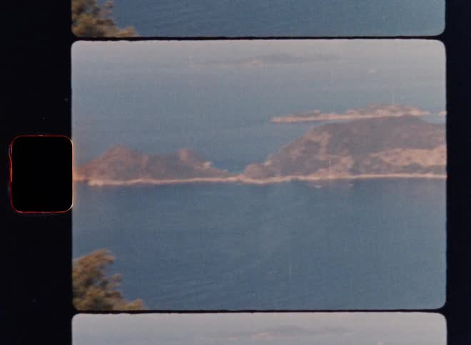 Cinematic Super 8mm coastal panorama: camera pans along a distant shoreline revealing a rugged, sea-surrounded peninsula, captured with nostalgic analog film grain for a vintage travel and landscape aesthetic