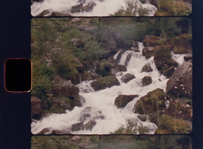 Framed as a film slide a static shot captures a powerful river creating a series of rapids as it cascades over mossy rocks in a lush forest