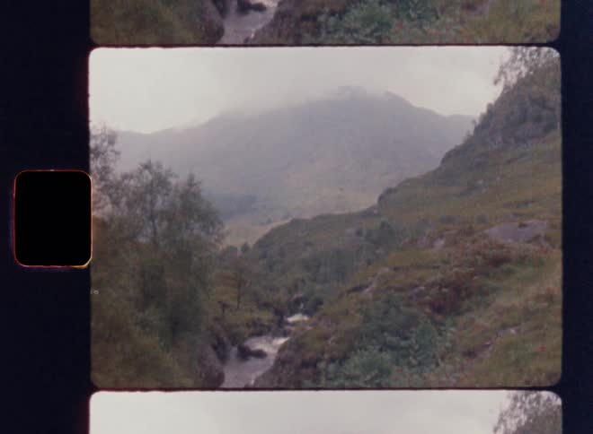 Framed as a film slide the camera tilts up from a rushing river in a gorge to reveal a large misty mountain in the distance