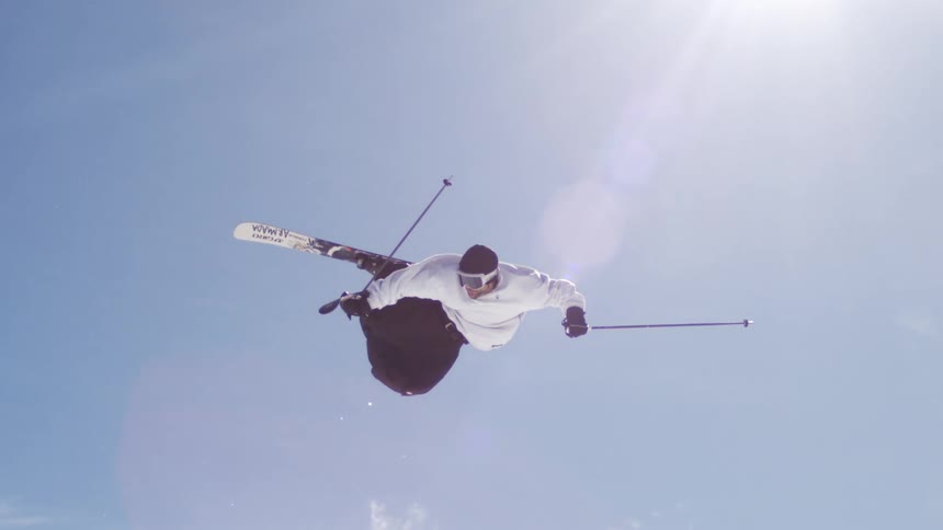 The video shows a person skiing jumping high in the air against a bright cloudy sky in the first half the camera is positioned to show the mountain in the background and then it shifts to focus only on the skier in the air the words filmsupply are