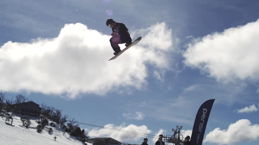 A super slow motion shot of a man doing a spin in the air on a snowboard and other people watching