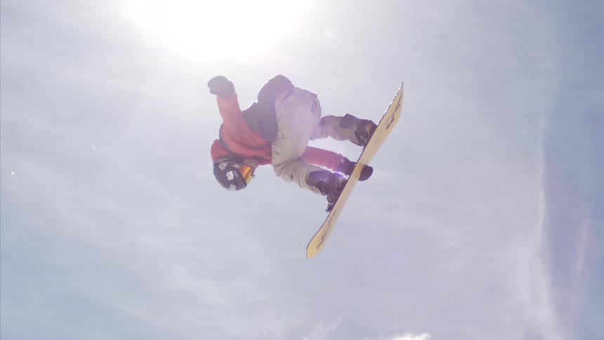 A person is doing a trick in the air using a yellow snowboard on a day with the sun shining in the sky