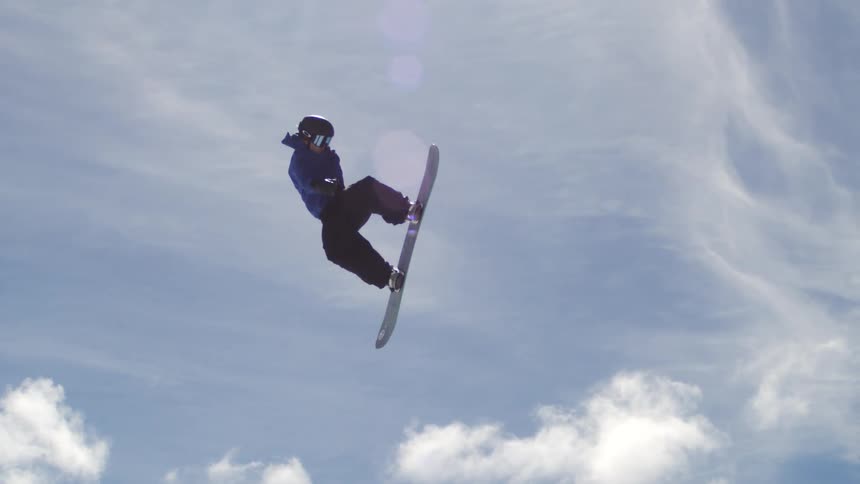 A snowboarder jumps high above a snowy ski slope at a mountain resort