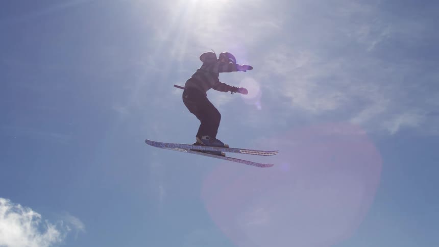 Ski rider wearing winter clothing and a helmet soaring into the air at midday on a sunny day in the snowy mountains