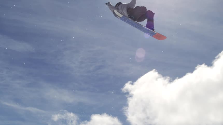 A snowboarder performs a high jump trick above a snowy ski slope
