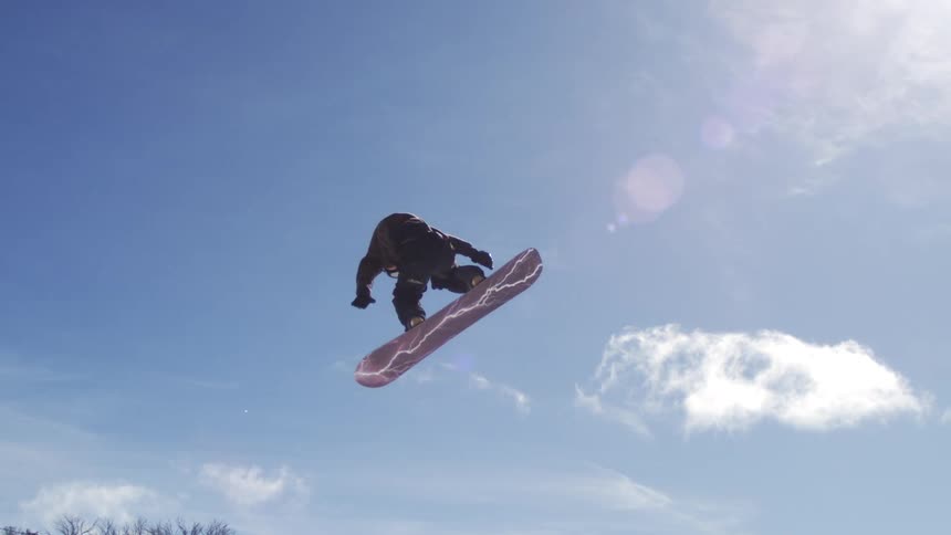 The man spins and jumps very high on a snowboard