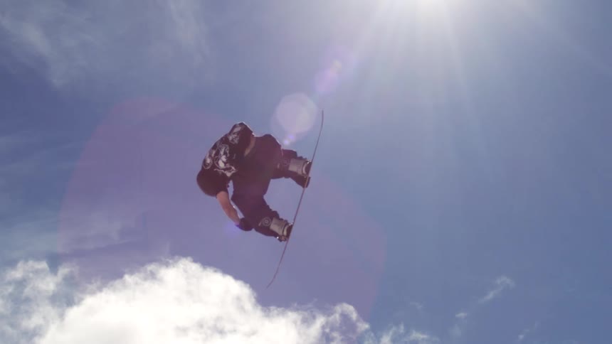 Snowboard rider in full snowboarding gear captured midair on a sunny winter day in the mountains performing an impressive stunt high above the snowy slopes