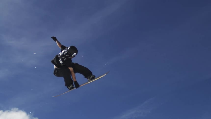 Snowboarder performing a jump trick rotates through the air before landing on the snowy ground on a winter day
