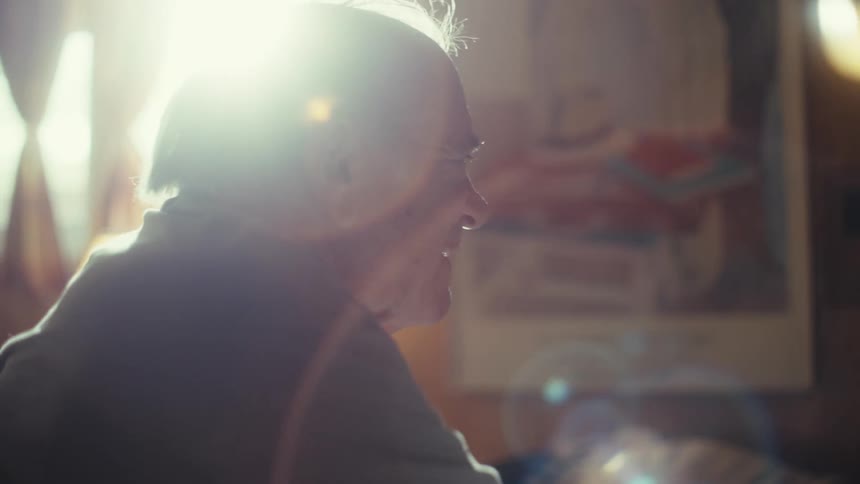 Elderly man cheers while watching television in a sunlit room