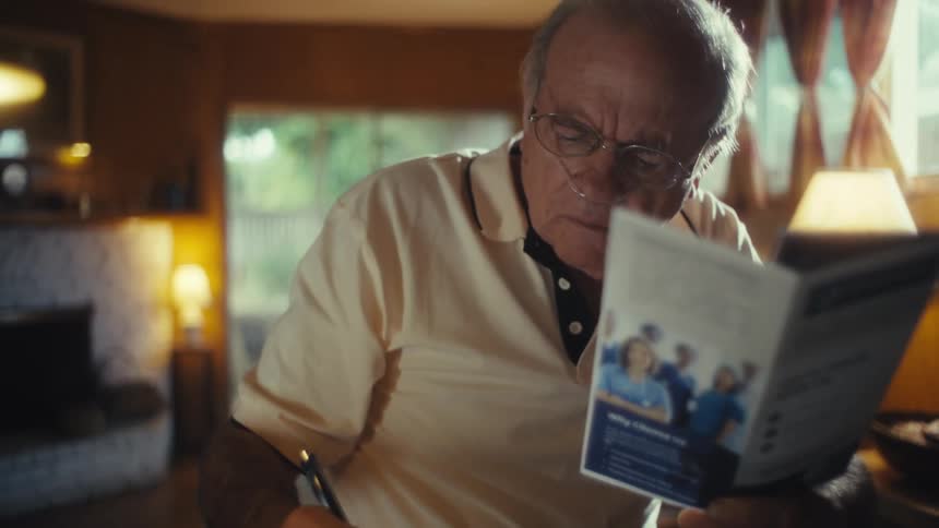 Elderly man reading a medical pamphlet while writing in a notebook