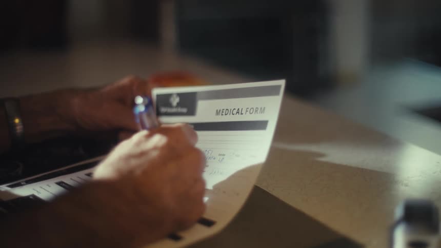 A person fills out a medical form with a pen at a desk
