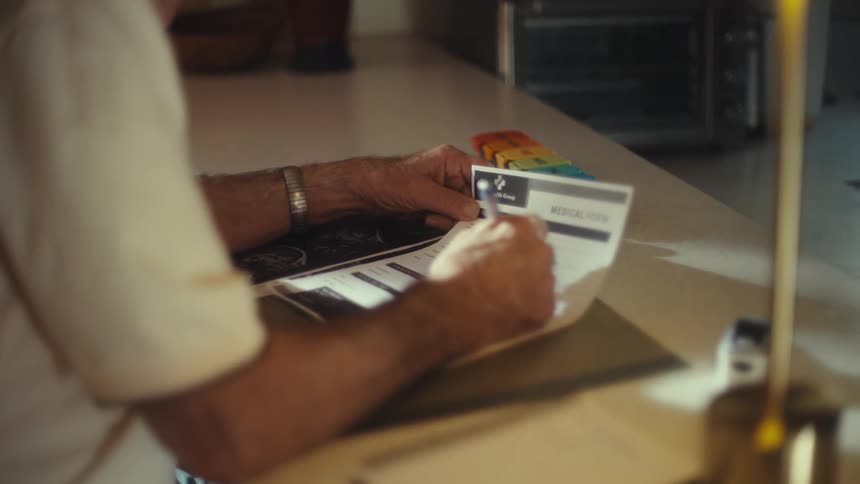 An elderly person fills out a medical form at a desk indoors