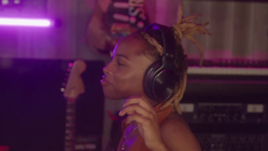 The woman holds her headphones while listening to music in the studio