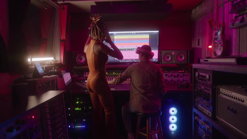 Woman with headphones singing in a studio next to a person sitting down