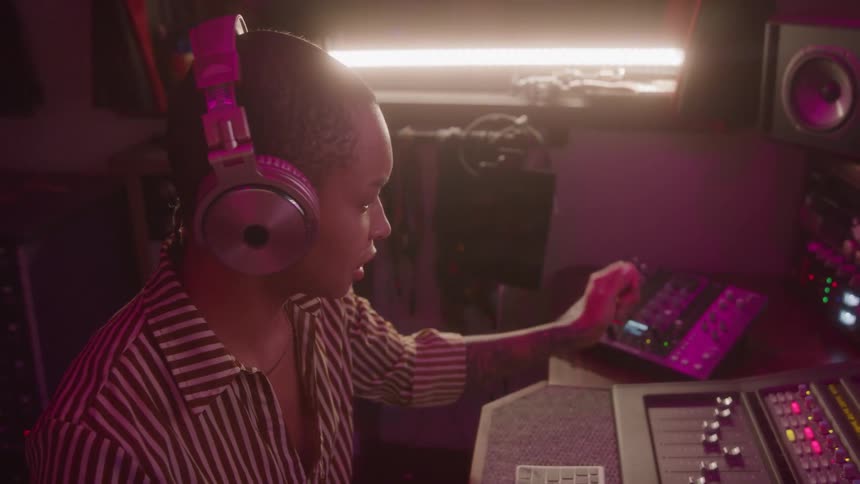 Young woman in a music studio wearing a headset nodding to the music while operating a mixer
