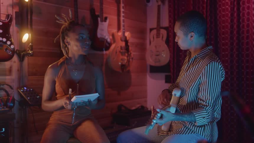Two women one with a notebook and the other with a guitar in a studio