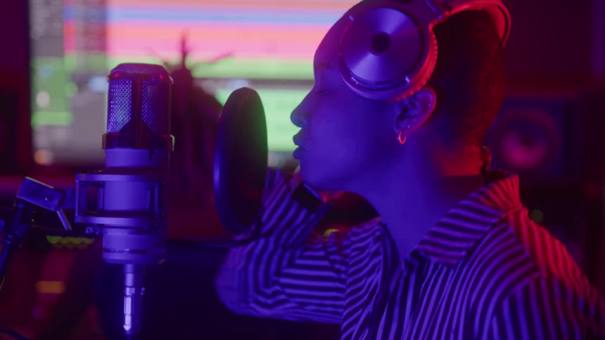 A person wearing headphones sings into a microphone in a vibrant colorfully lit recording studio