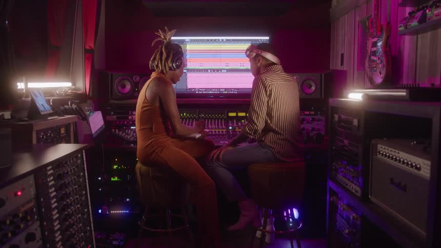 Two women collaborate in a recording studio in front of the audio editing screen