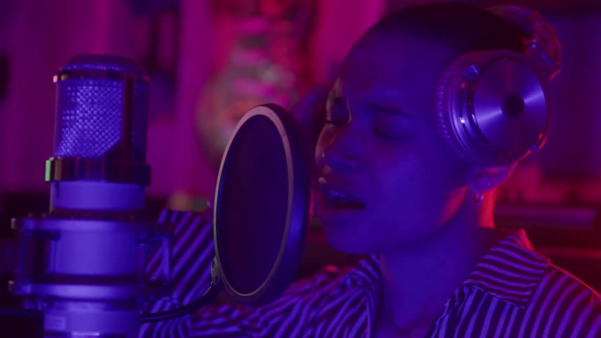 Young woman in a music studio wearing a headset singing passionately into a recording microphone during a session