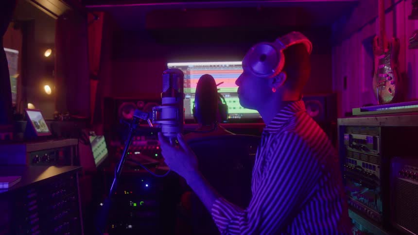 Woman sings facing the microphone in a studio with a mixing console