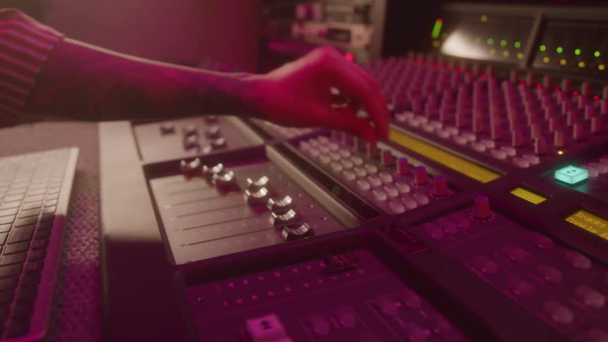 A persons hand pressing a button on a mixing console with pink lights