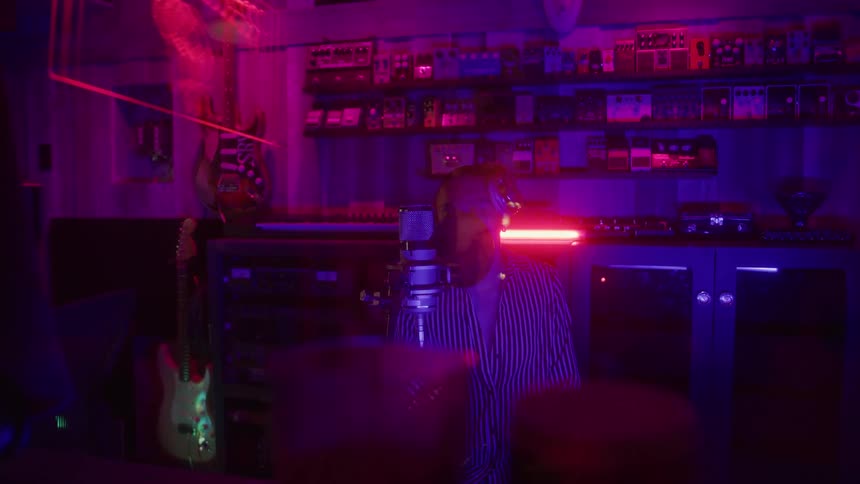Person in a studio lit by purple lights singing into a microphone