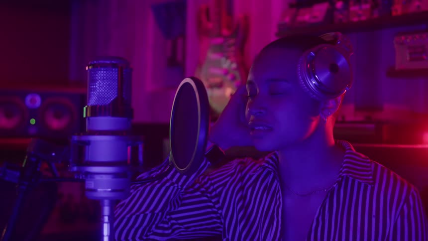 Young woman in a music studio wearing a headset singing passionately into a recording microphone during a session