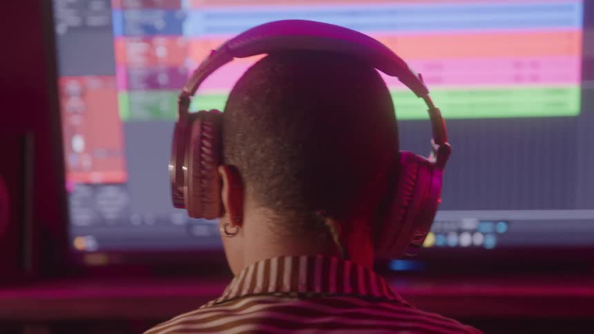 The back of a persons neck with short hair and with headphones in their ears shaking their head while listening to music