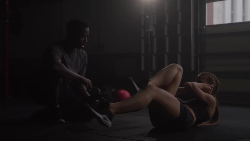 Athlete performs an abdominal exercise on the floor with the trainers supervision