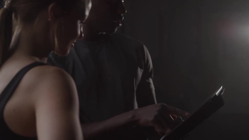 Personal trainer shows guidance on a tablet to a trainee during workout