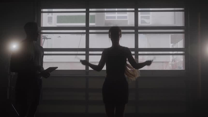 The silhouette of a woman jumping rope indoors with a window behind