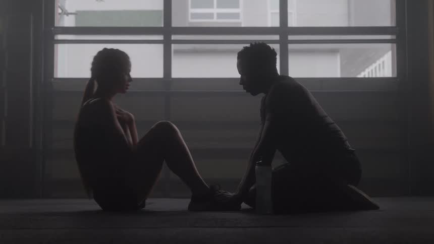A woman is lying on the floor doing situps while a man holds her feet for support and then they give each other a high five and she drinks water