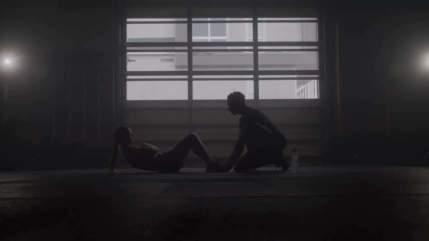 Athlete performs situps on the floor with the support of the trainer inside the gym