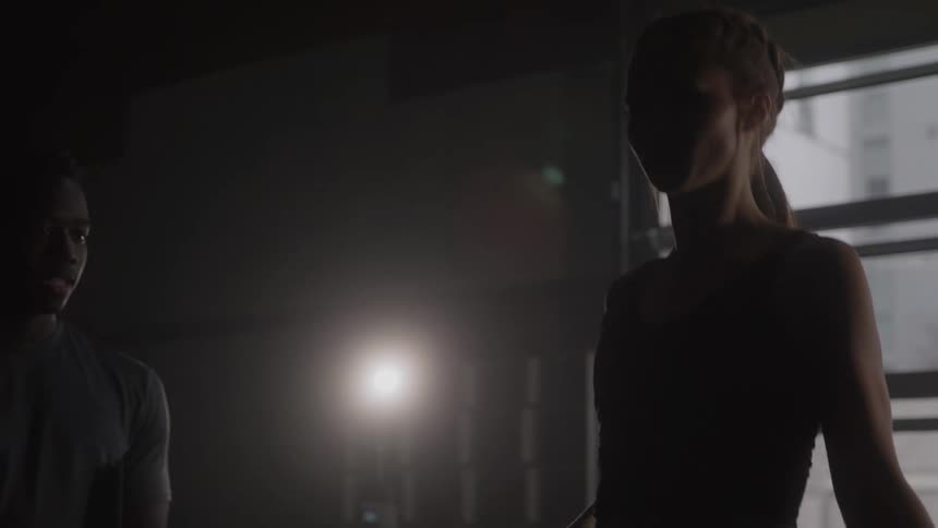 A woman trains with a jump rope alongside her instructor in a dimly lit gym