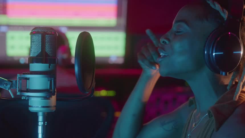 Singer wearing headphones records vocals in a studio in front of a professional microphone