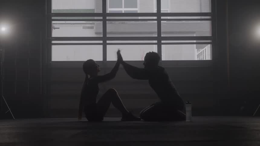 A woman is doing situps while a man holds her feet and then they high five and the man hands her a bottle of water