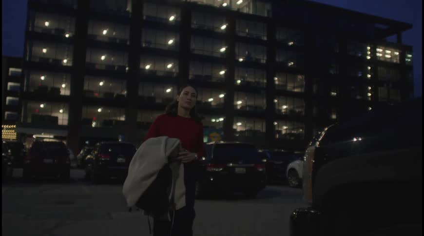 Young woman holding a coat walking through a parking lot in a residential area at night