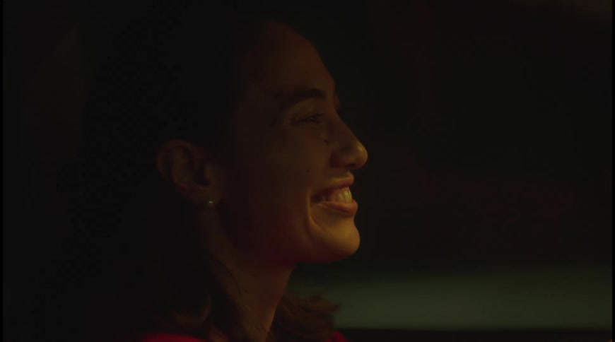 An asian woman with short hair is driving a car at night and laughing