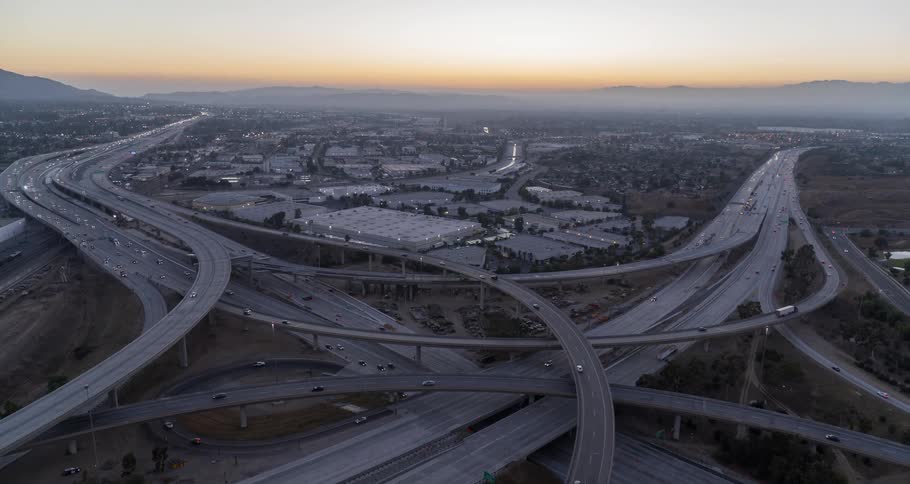 Traffic travels on a networkof multi level highways while red tints the horizon on a foggy morning