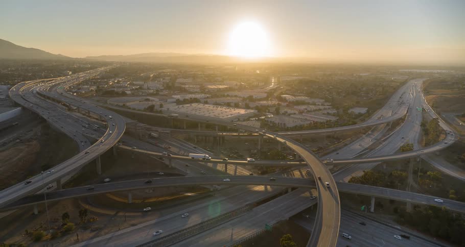 Aerial view of multiple interconnected overhead bridges feeding into and out of an interstate highway bathed in the warm glow of an orange setting sun with cars moving steadily in both directions