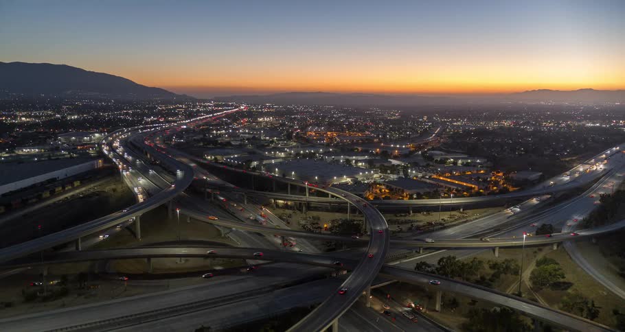 Aerial view of a busy highway interchange at sunset with city lights in the background