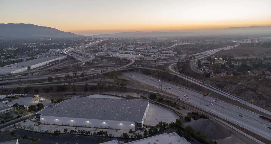 Aerial view of a highway interchange at sunset with buildings and mountains
